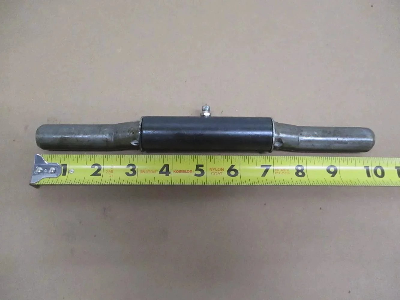 Single weld-on trailer ramp door hinge with integrated grease fitting next to measuring tape, 1x10 inch size, raw 9-gauge steel construction.