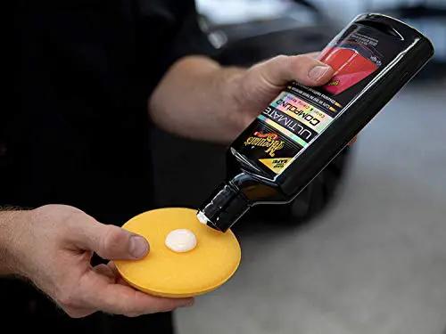 Hand holding a bottle of Ultimate Compound For Cars That Removes Oxidation Swirl Marks Water Spots And Scratches On Clear Coat with applicator.