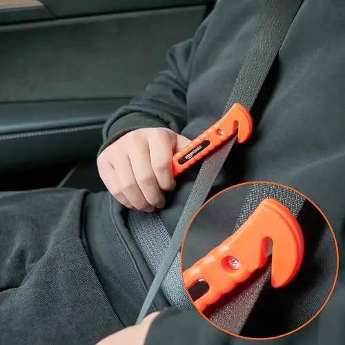 Close-up of bright orange seatbelt cutter from Emergency Escape Tool Kit With Window Breaker And Seatbelt Cutter For Cars Bright Orange Safety Hammer In Protective Bracket 2 Pack Tungsten Head Non Slip Grip SW-835, being held against a seatbelt.
