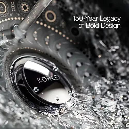 Close-up of water flowing over a silver Kohler drain, showcasing intricate swirling design and text '150-Year Legacy of Bold Design'.