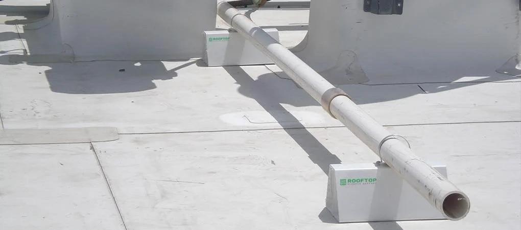 4 Pack 6 Inch Pre Cut PVC Rooftop Pipe Support Blocks For Roof Piping supporting a white pipe on a flat rooftop surface.