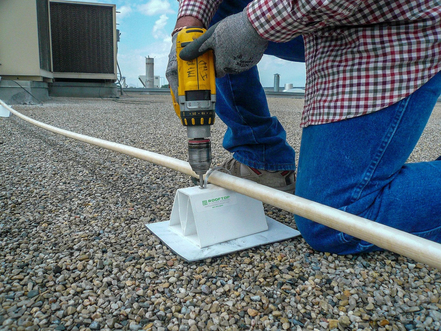 Person installing 4 Pack 6 Inch Pre Cut PVC Rooftop Pipe Support Blocks for roof piping on a gravel surface.