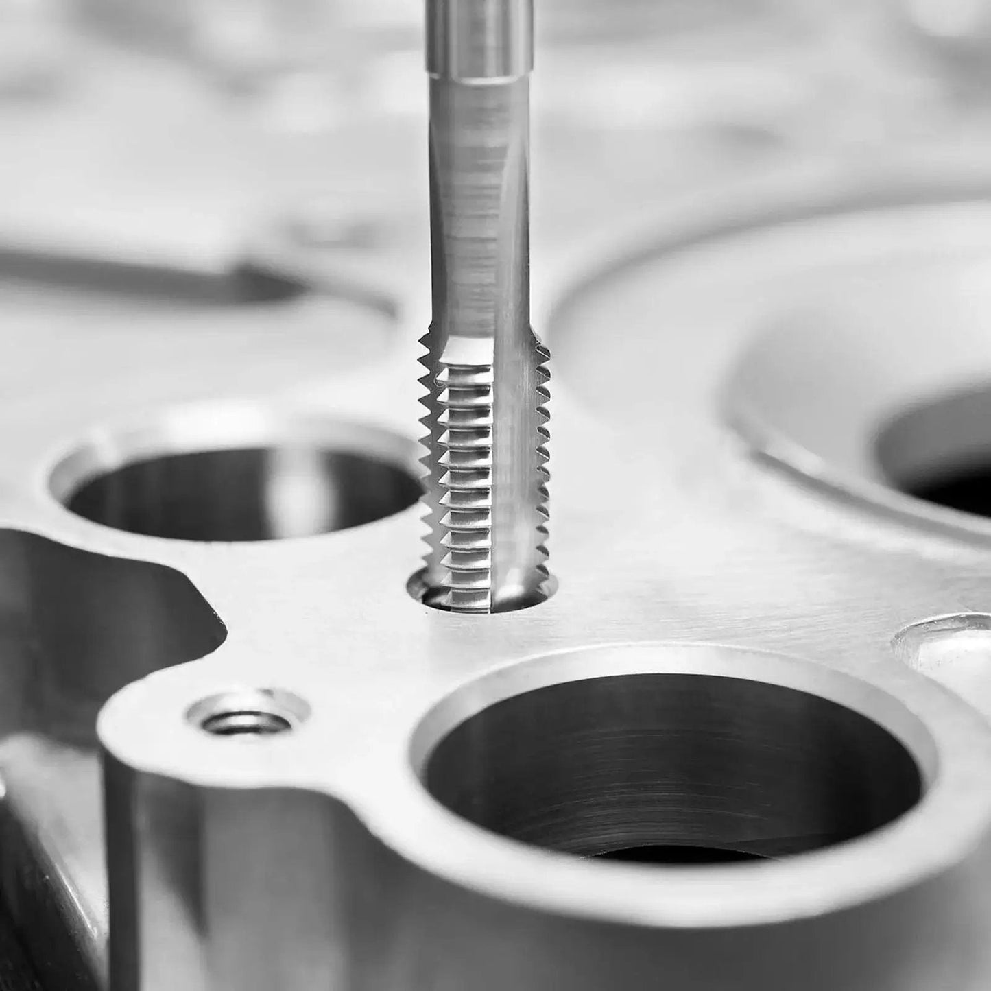 Close-up of a hardened steel tap from a 116 Piece Tap And Die Set For Metric And SAE Threads With Hardened Bearing Steel Taps And Dies Includes Full Accessories And Storage Case For Cutting External And Internal Threads In Tough Work Environments cutting threads in metal.
