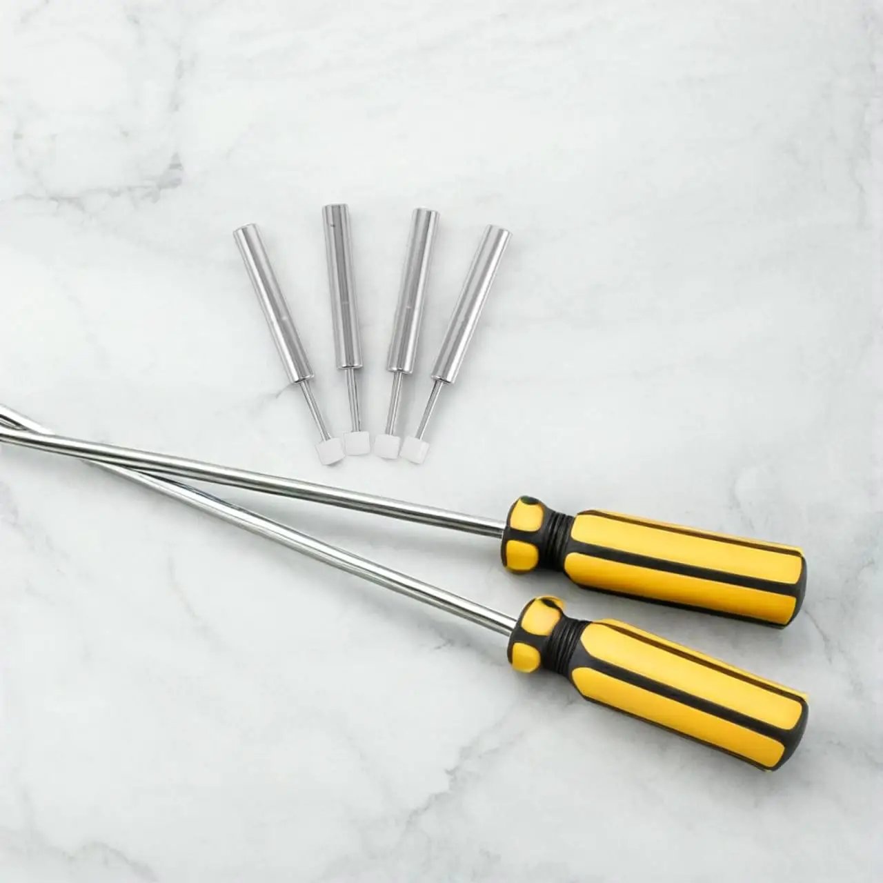 Two yellow-handled magnetic screwdrivers with four interchangeable bits on marble surface