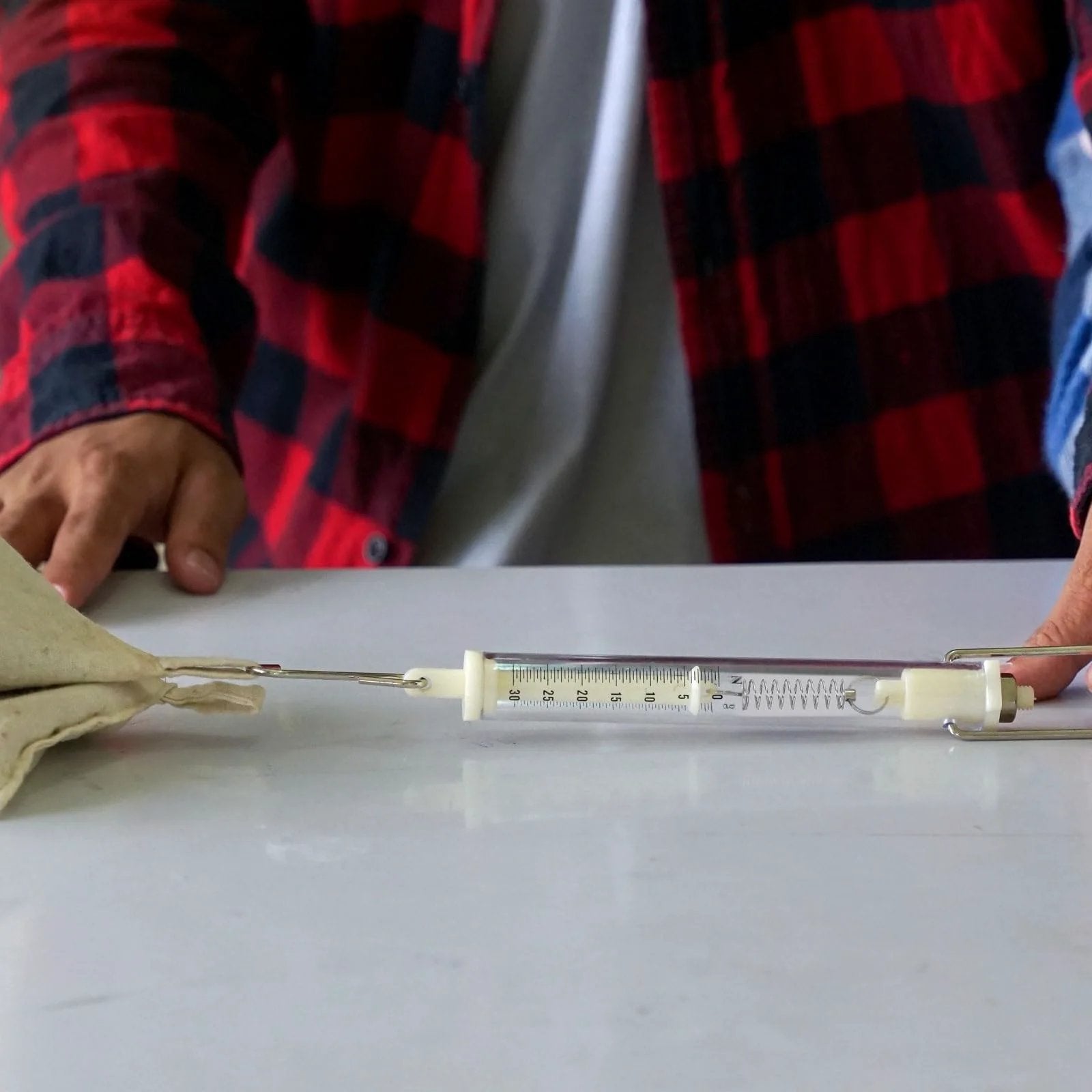 Person using a mechanical extension spring attached to a syringe on a table.