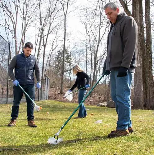 People using the 36 Inch Nifty Nabber Reacher Grabber Tool for easy yard cleanup and trash pickup in a grassy outdoor area.