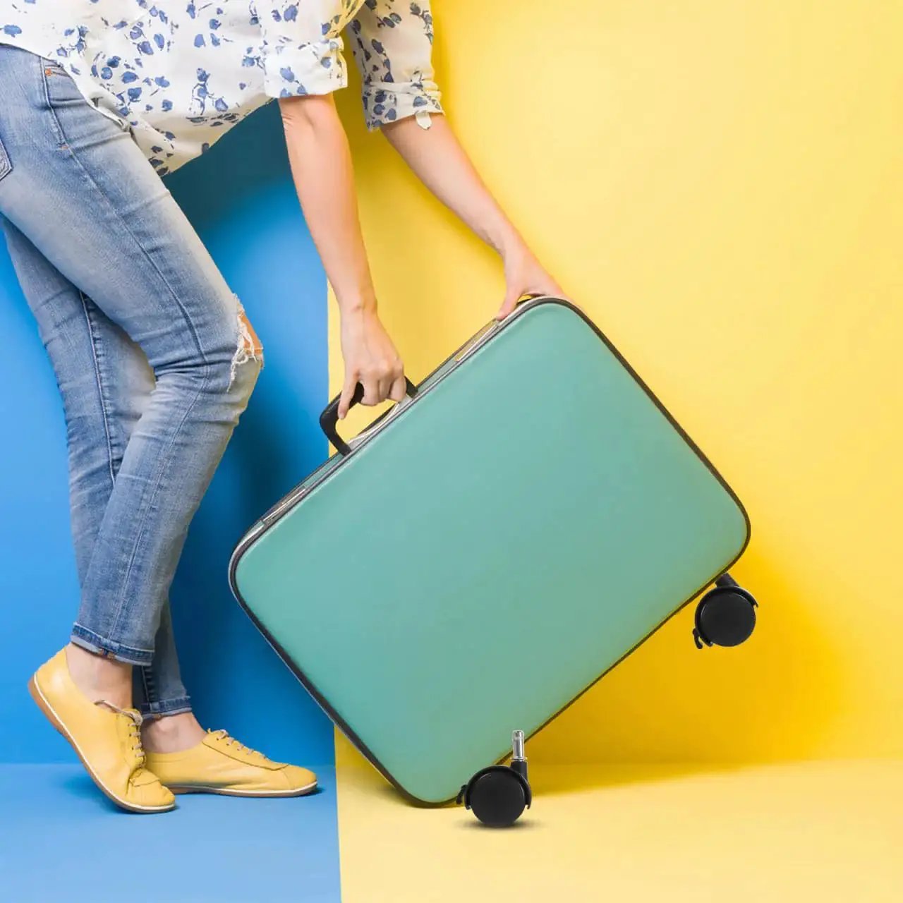 Person holding a teal suitcase with black swivel caster wheels on a blue and yellow background