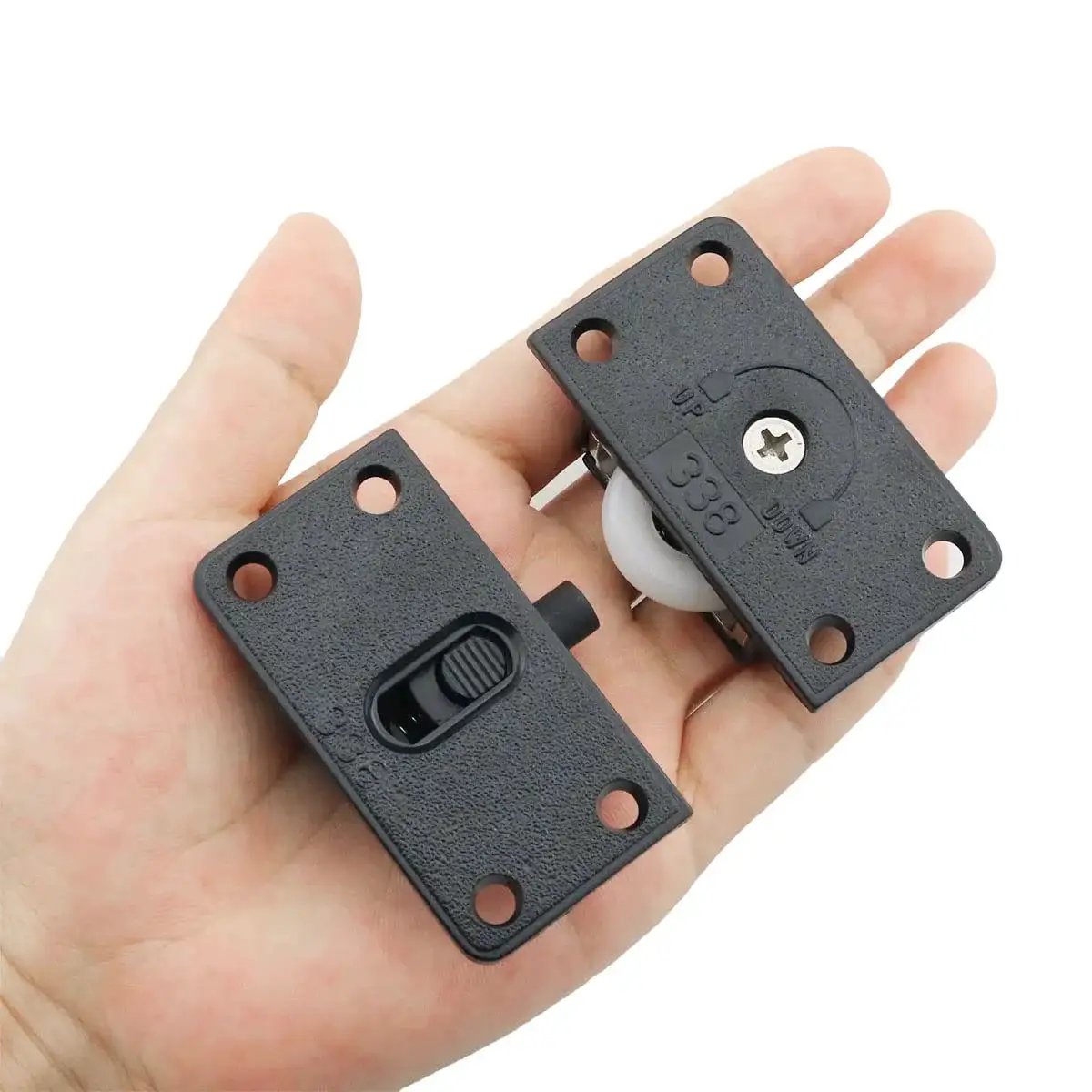 Person holding two sets black sliding cabinet hardware components with nylon pulley wheels, hand showing size and design details.
