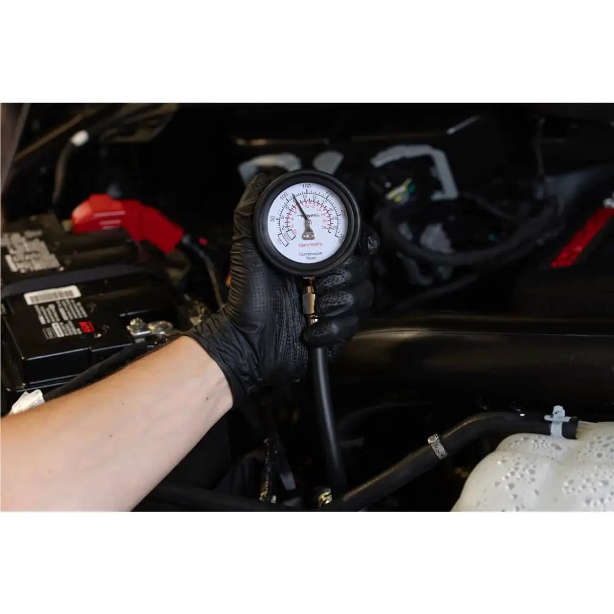 Person holding Engine Compression Test Kit With 2.75in Gauge And Quick Disconnect Adapters inside a car engine bay