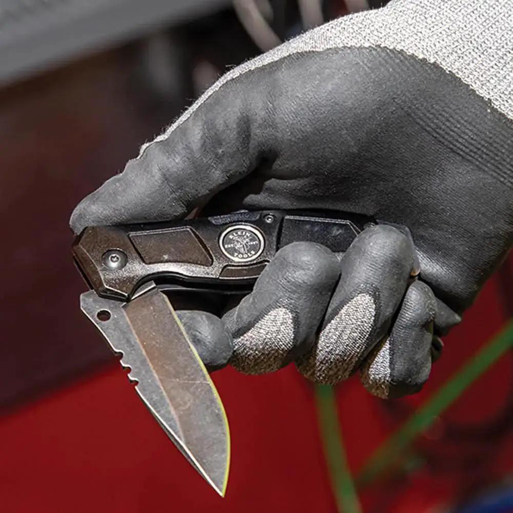 Gloved hand holding Folding Pocket Knife For Electricians With Bearing Assist Flipper And Frame Lock Black Handle Drop Point Stainless Steel Blade