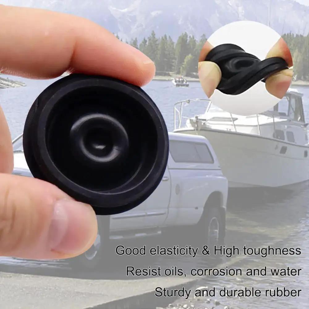 Close-up of a black rubber trailer hub cap plug held in hand, showing elasticity, for 1.98 inch hubs; background shows trailer and boat.