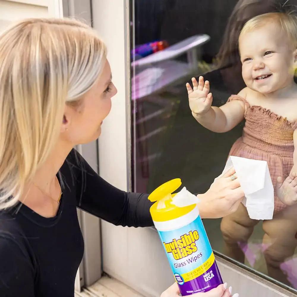 Woman using Pack Of 3 Pre-Moistened Glass Wipes, Streak-Free And Lint-Free For Windows to clean a glass door with a smiling baby.