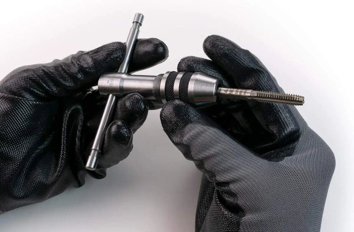 Two Piece Tap Wrench Set with Sliding T Handle and Reference Table for Zero to One Half Inch Taps held in gloved hands