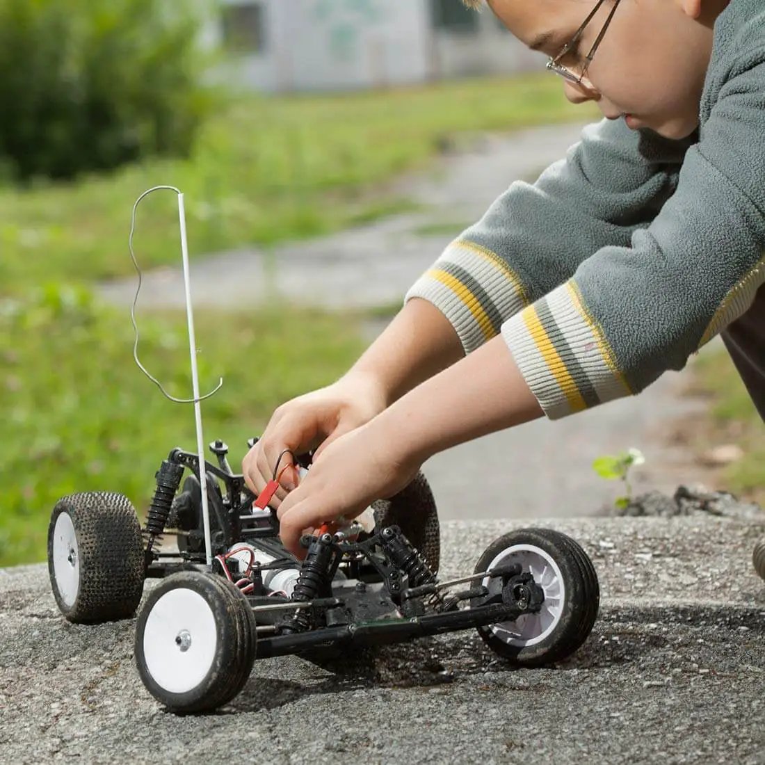 Child adjusting a remote control car on a concrete surface outdoors.