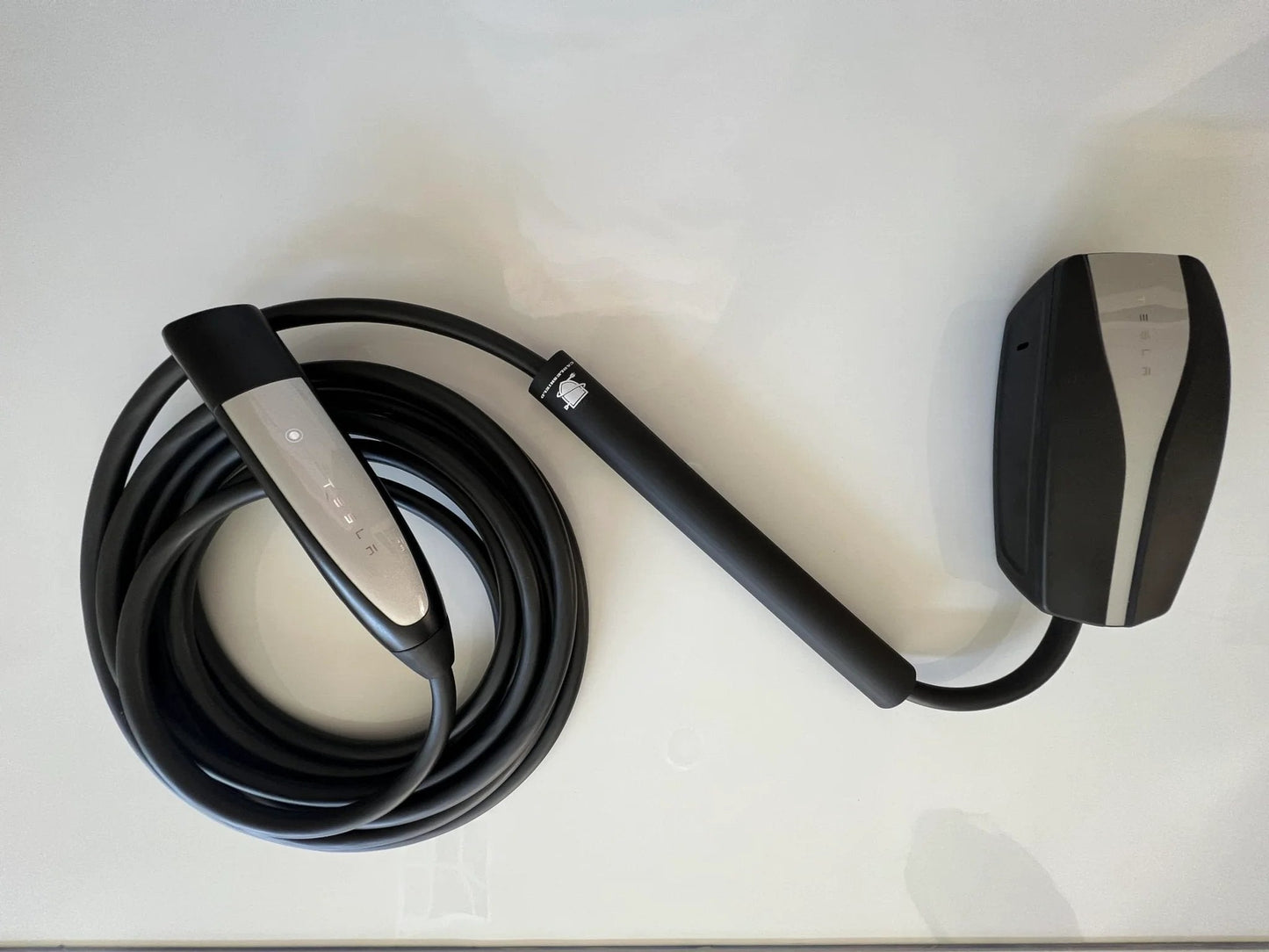 Durable EV Cable Protector For Garage Pass Through 0.5 Inch ID Large, Tool-Free Install Shields Your Charging Cable From Doors, Cars, And Wear, US Made, Easy Protection For Tesla Home Wall Connector And Tesla Mobile Connector Cables showing a black coiled charging cable with a connector.