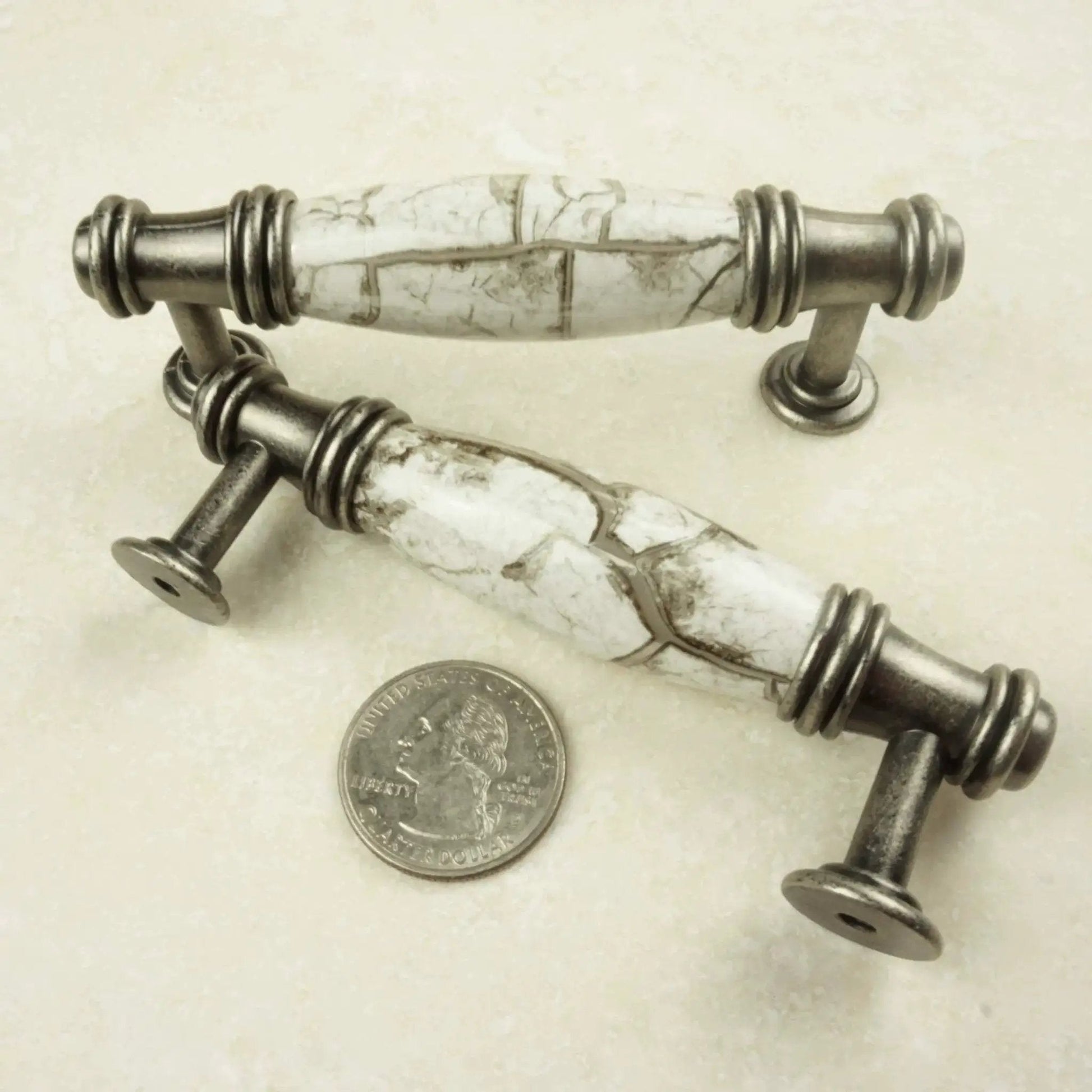Antique silver white marble cabinet pulls with quarter for scale, detailed design.