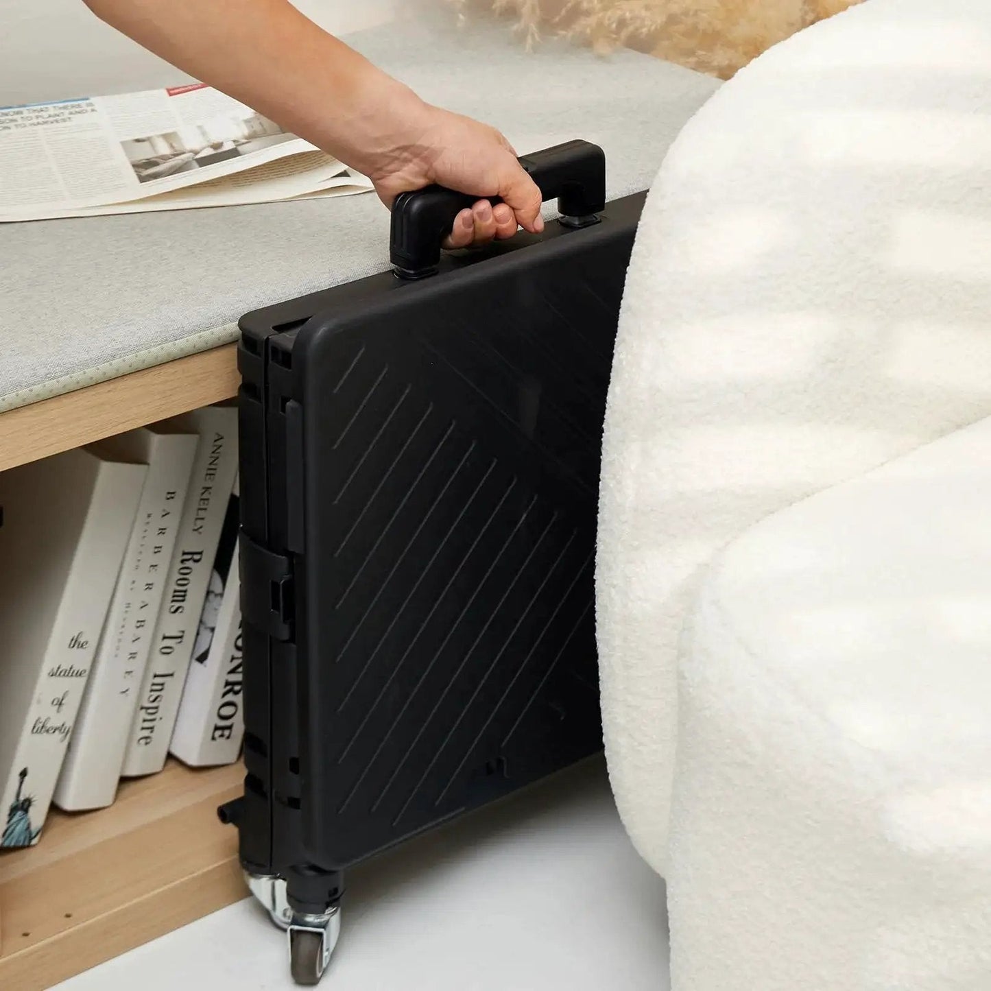 Compact black folding utility cart with lid and basket on four 360 degree rotating wheels, stored upright under a table.