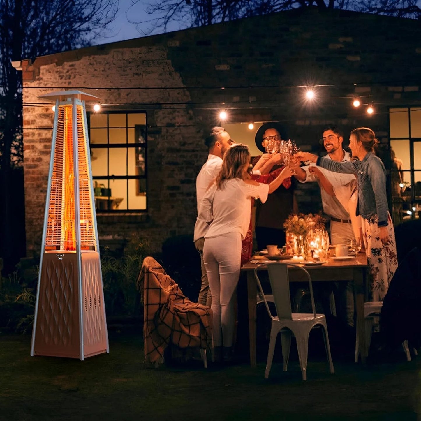 Group of people enjoying a dinner outdoors with a tall propane patio heater and string lights in a garden setting at night.