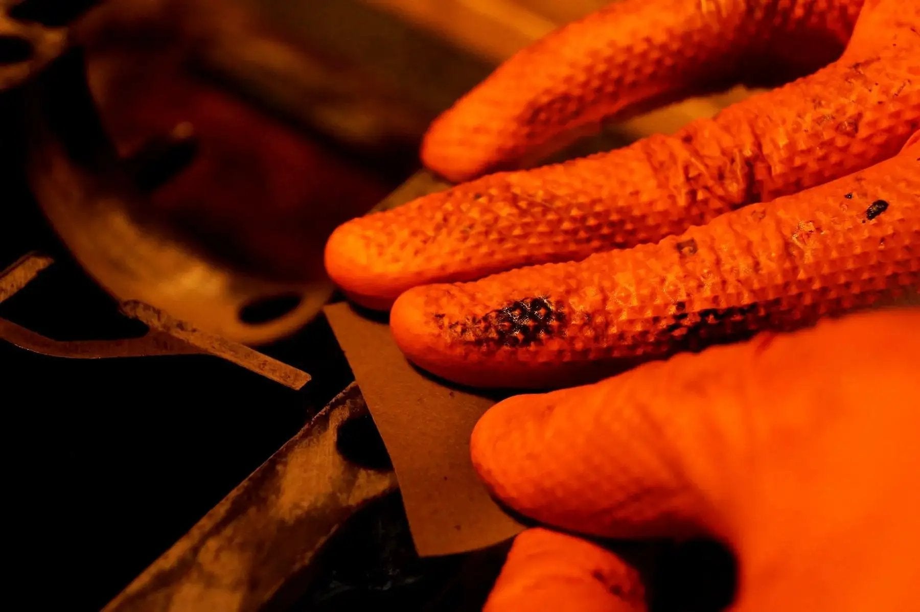 Close-up of hands wearing 8 Mil Orange Nitrile Gloves With Diamond Textured Grip For Industrial And Food, working on machinery.