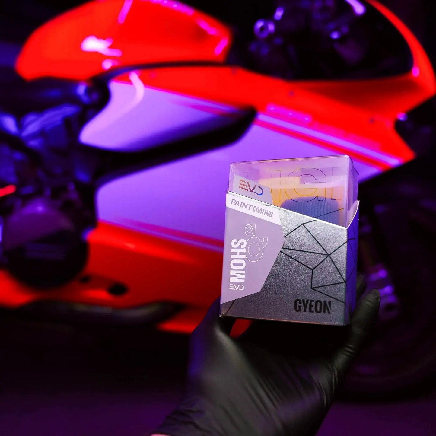 Gyeon Mohs Ceramic Coating Kit For Cars DIY Deep Gloss And 3 Year Protection held in gloved hand with a motorcycle in background