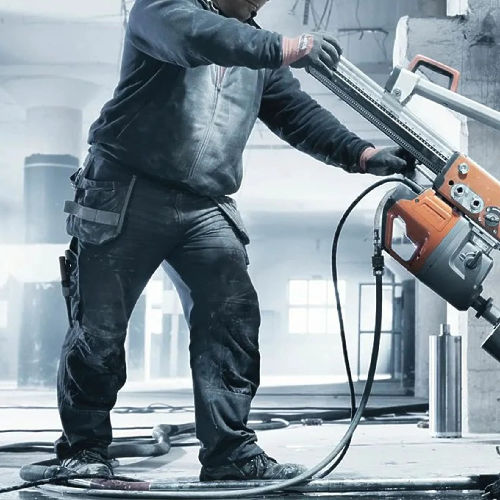 Person operating a construction tool indoors, wearing work attire. Tool is connected to a hose, used for construction tasks.