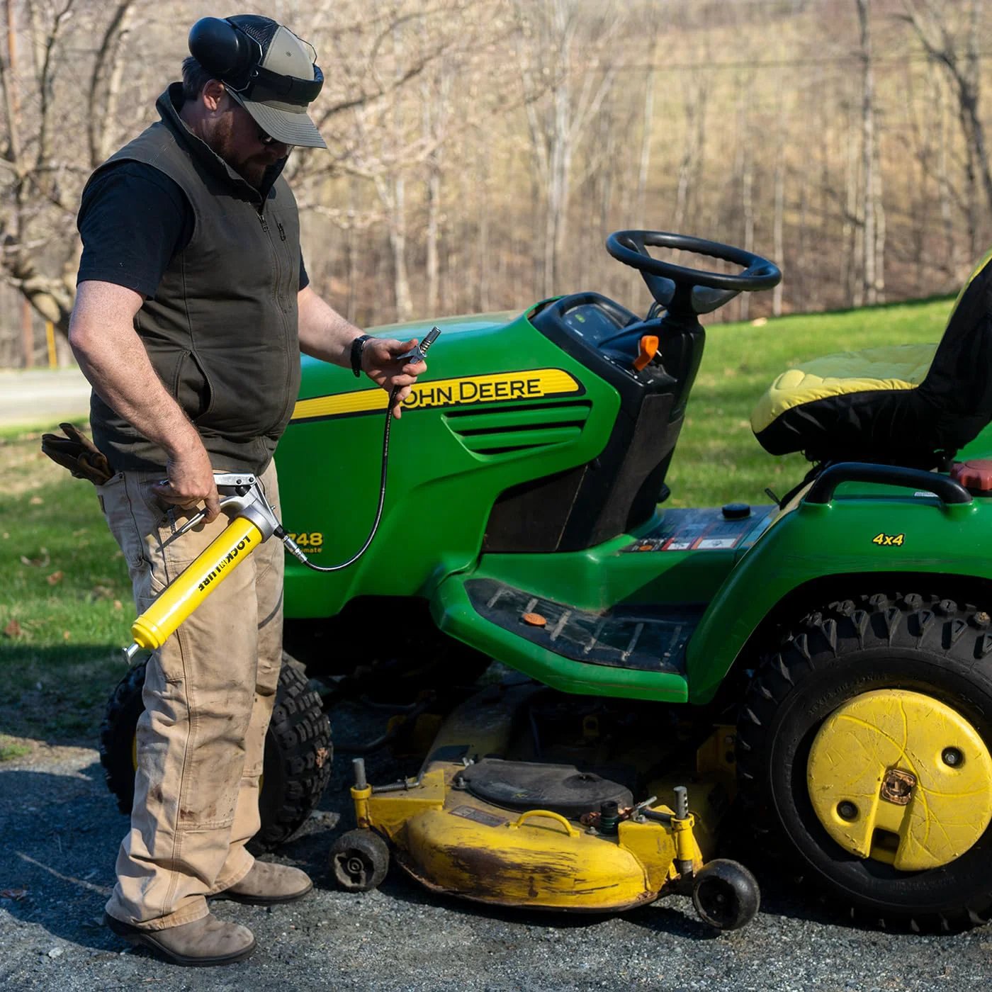 Man using Premium Pistol-Grip Grease Gun With LockNLube Coupler, 20 Inch Hose And Inline Swivel on lawn tractor for lubrication