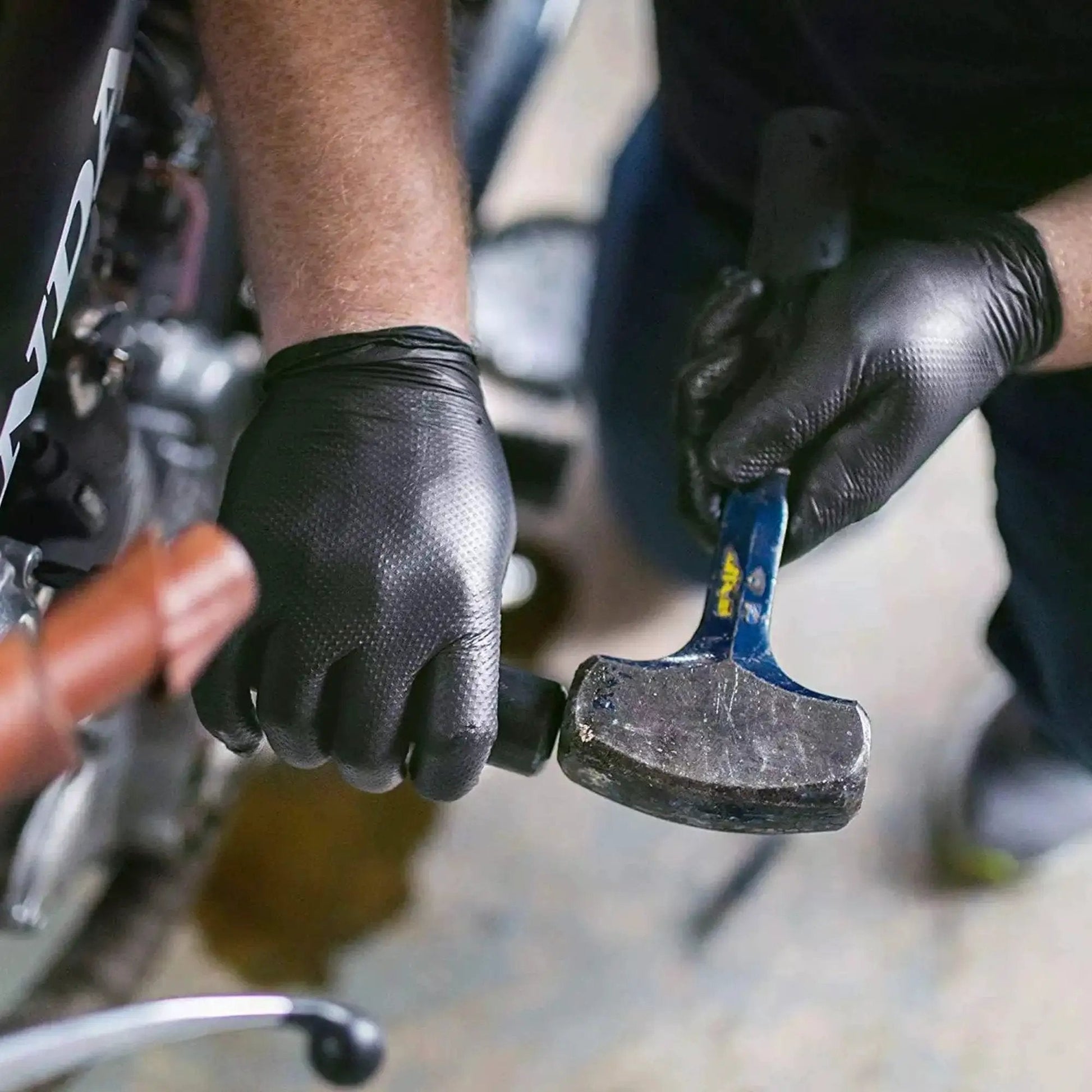 Mechanic wearing Heavy Duty Black Nitrile Gloves 8 Mil XL With Diamond Texture And Powder Free using a hammer