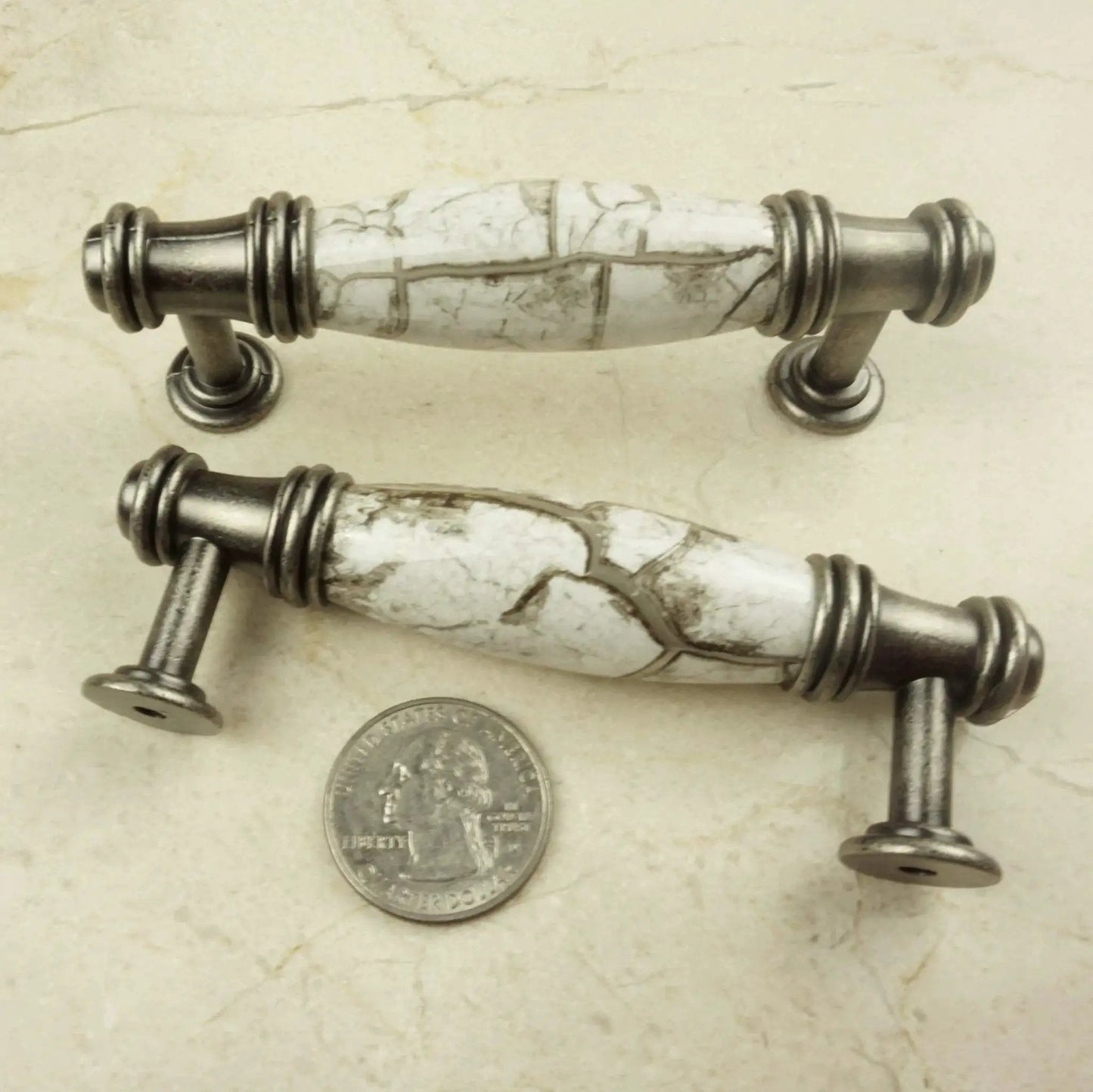 Two decorative cabinet pulls with marble-look design and silver hardware next to a quarter for scale.