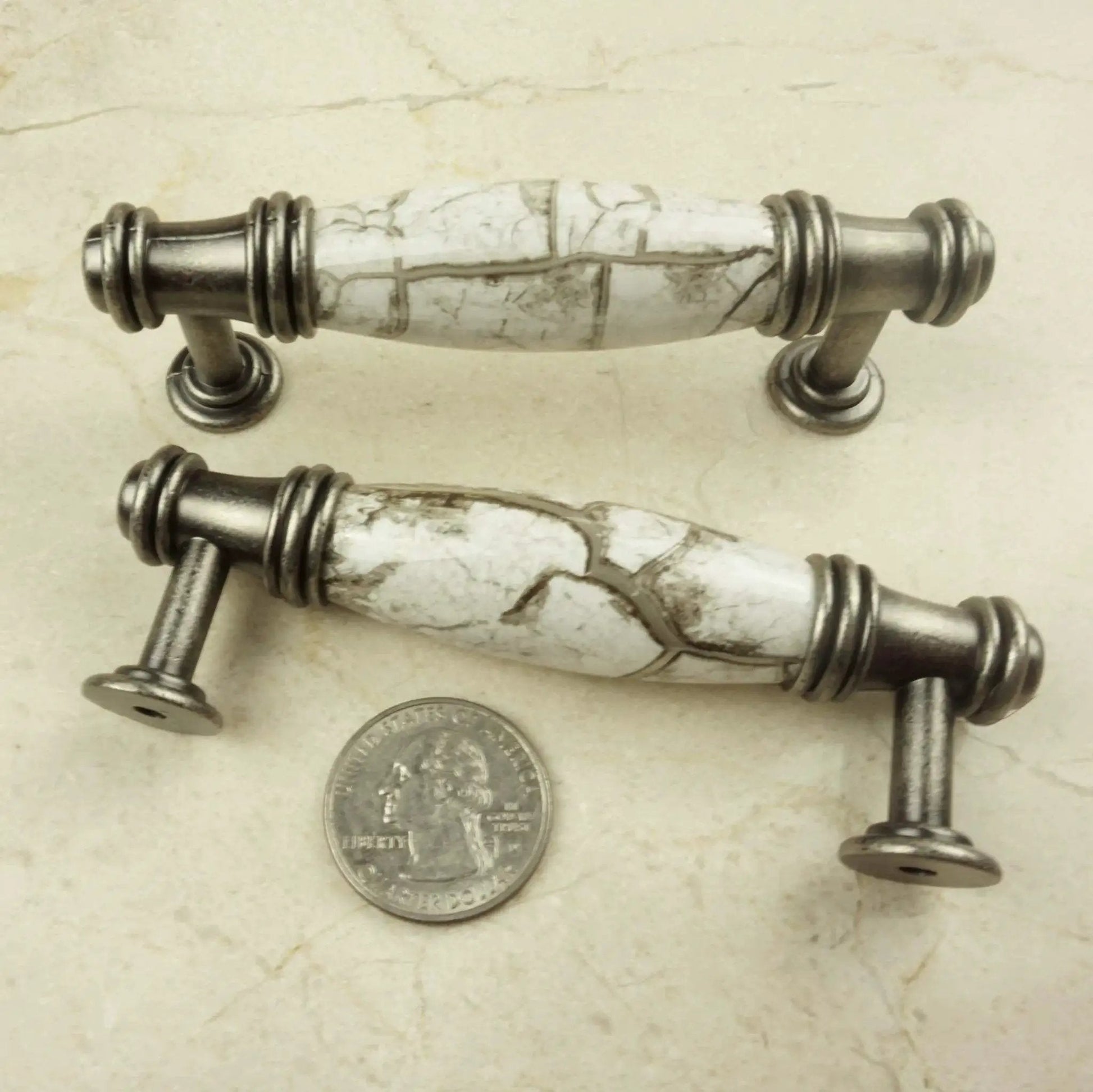 Two decorative cabinet pulls with marble-look design and silver hardware next to a quarter for scale.