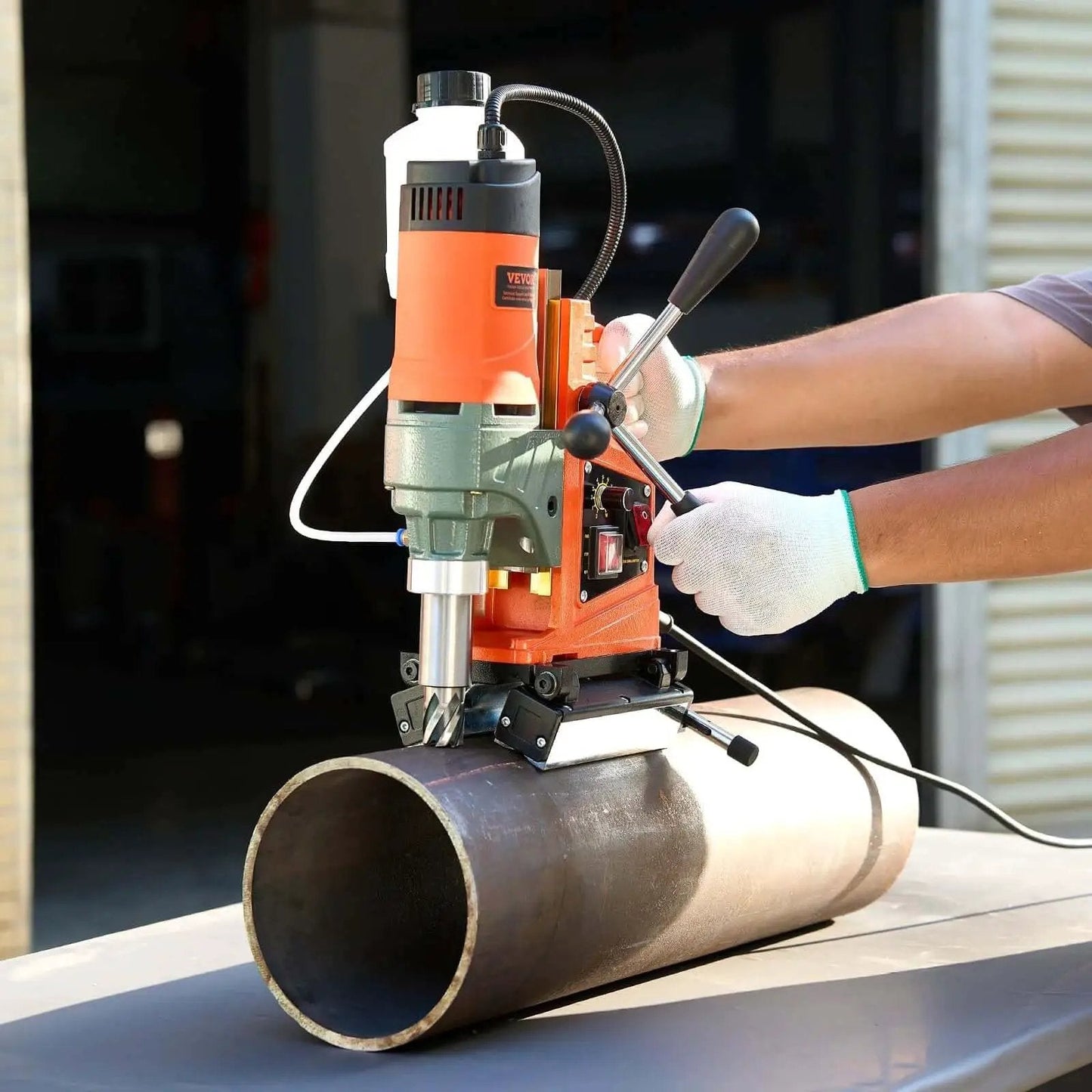 Magnetic Drill Press Workhorse With 1400W Power 2 Inch Boring Diameter 0 To 750 RPM Variable Speed Reversible Direction Includes 6 Core Bits Electric Mag Drill for Industrial and Home Improvement Projects in use on a metal pipe.