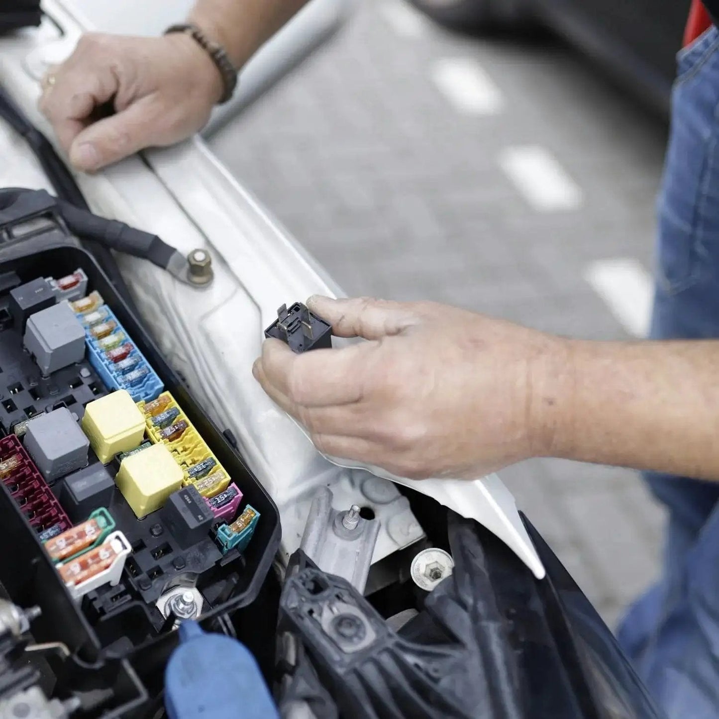 Mechanic examining car fuse box in automotive setting with tools, emphasizing automotive hoses repair