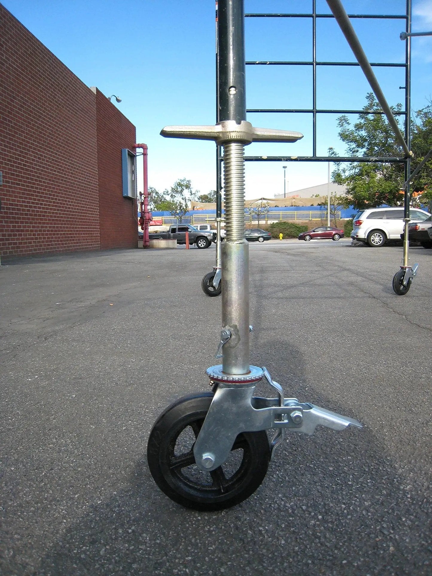 Side view of Set Of Four Eight Inch Caster Wheels With Cast Iron Hubs And Locking Brakes CBM1290 attached to scaffold on outdoor pavement.