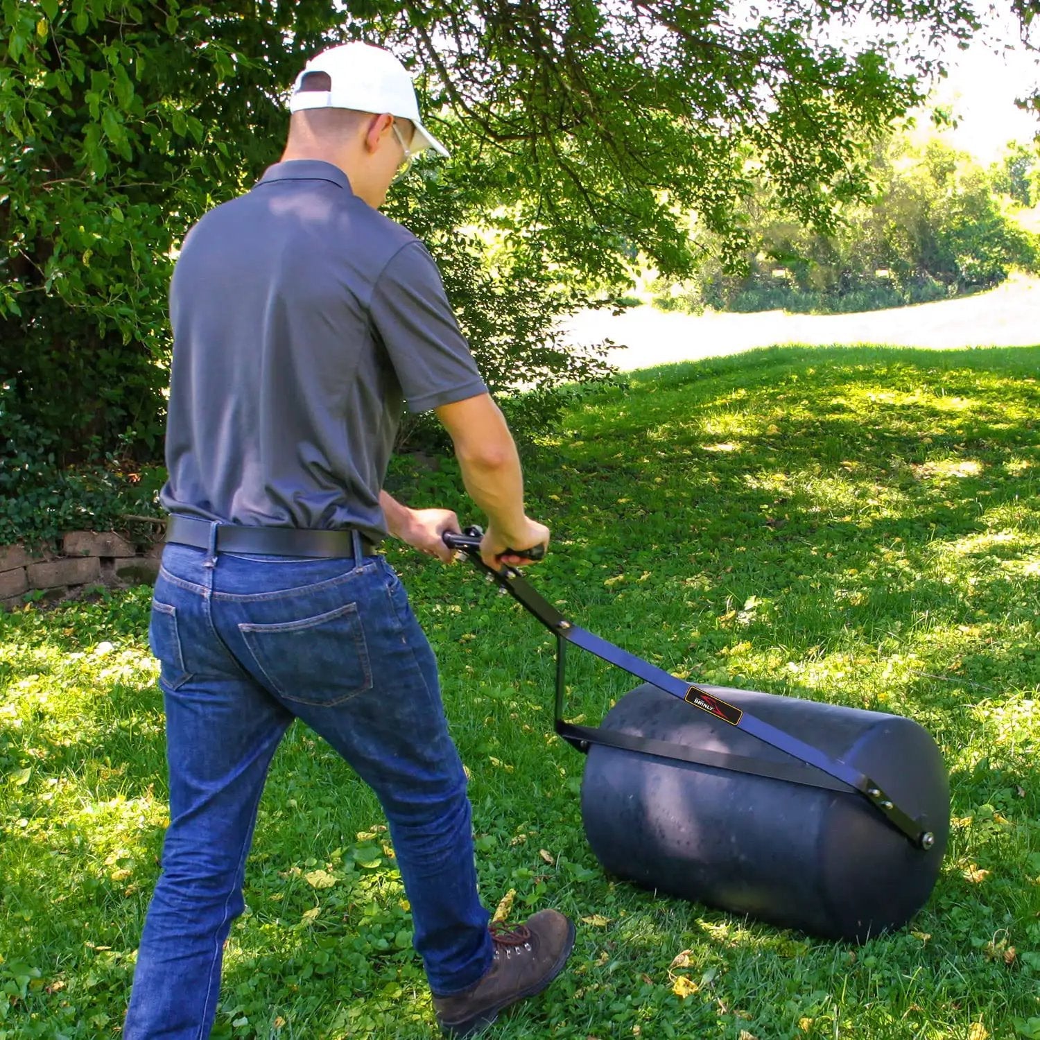 Person using powerful 270 lb poly lawn roller for push or tow with easy turn tethered plug and quick filling drum in garden