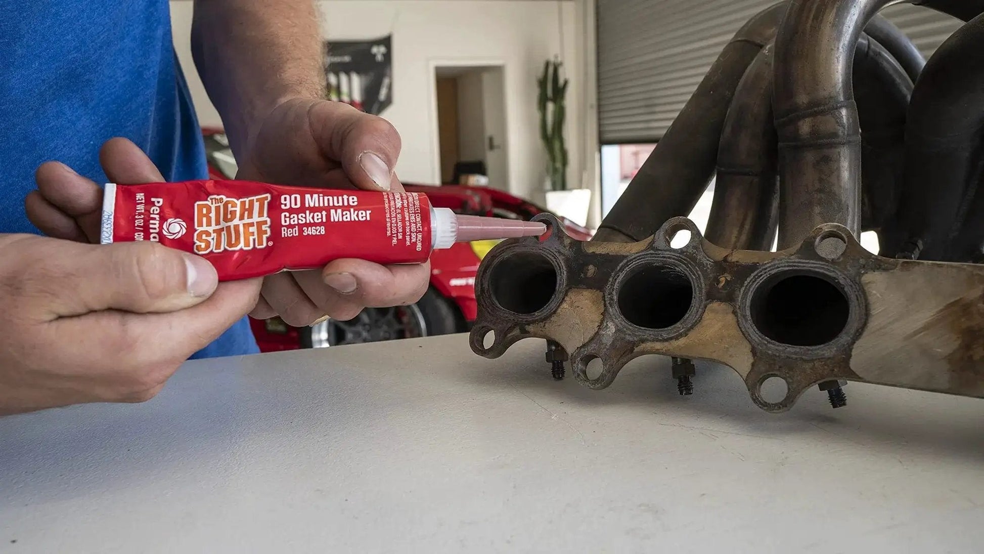 Person applying Right Stuff 90 Minute Red High Temperature Gasket Maker For Headers And Exhaust, 3 Oz Tube to exhaust manifold