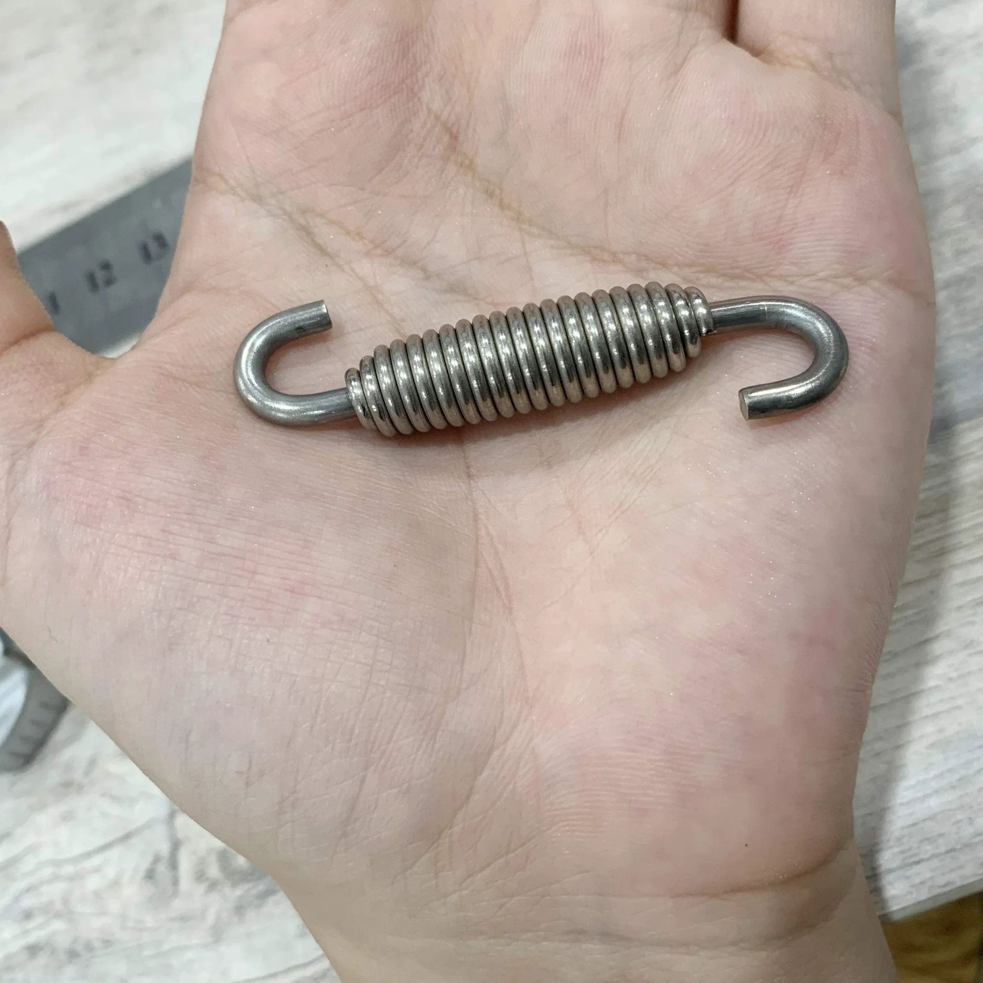 Hand holding Motorcycle Exhaust Spring Set 4 Pack Stainless Steel Swivel Hook Springs 58mm Long For Mufflers