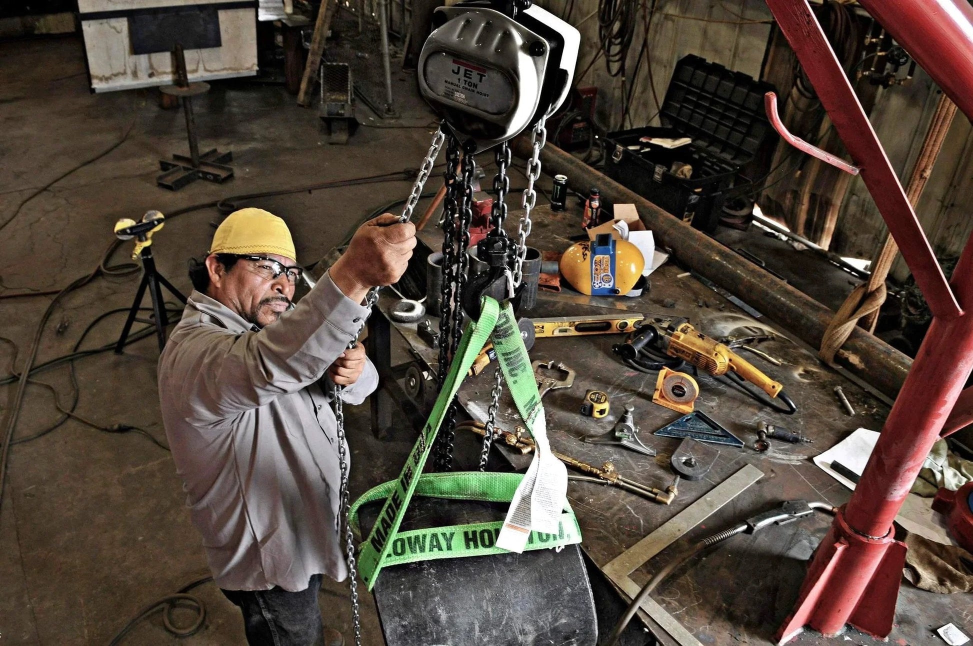 Worker using a 1 Ton Hand Chain Hoist For 10 Foot Lift Model S90 100 10 Gray With Industrial Rated Alloy Steel Hooks in a workshop.