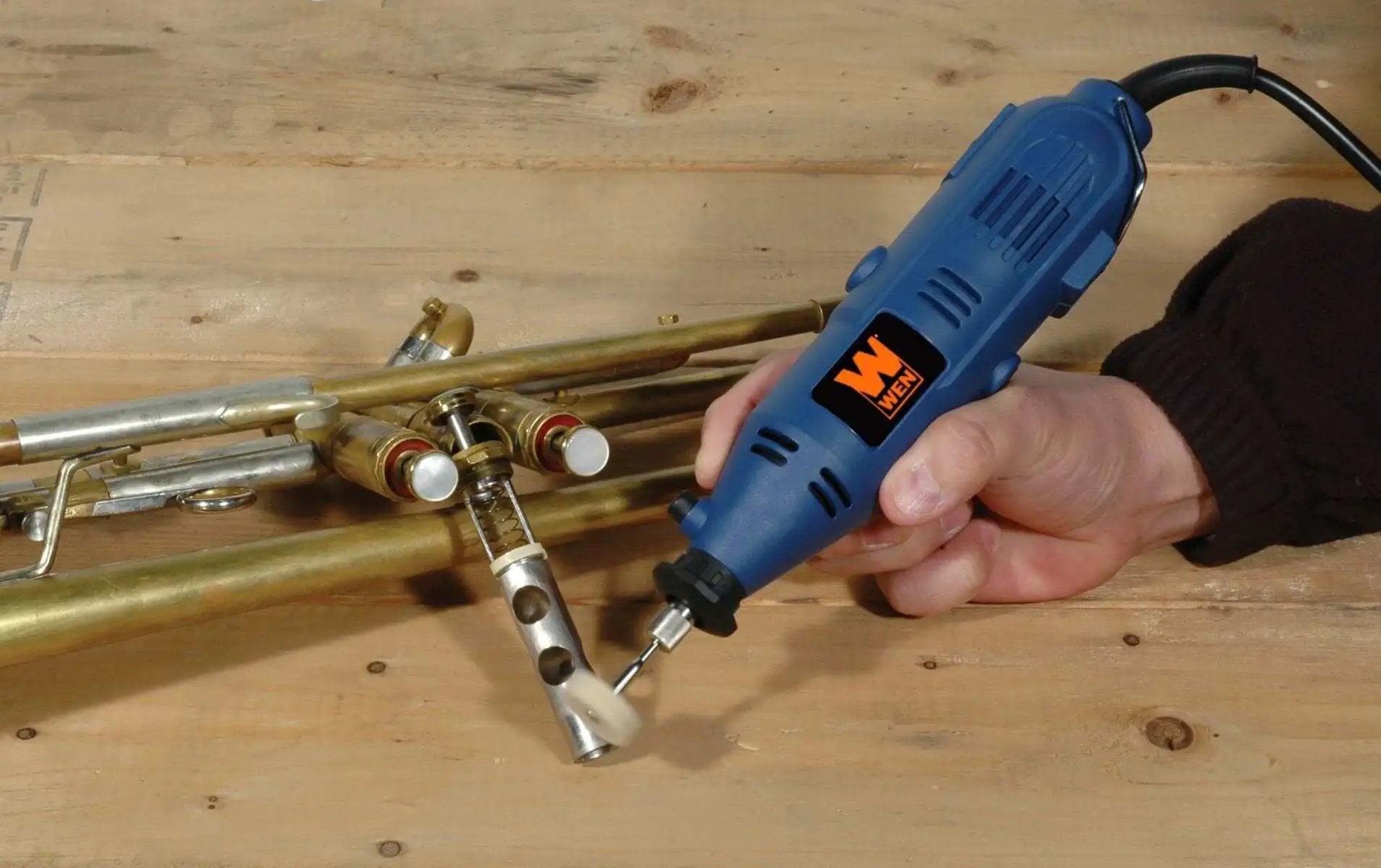 Person using All Purpose Rotary Tool Kit With Flex Shaft From WEN, 80 Piece Accessory Set, Variable Speed 8000 To 30000 RPM on brass instrument.