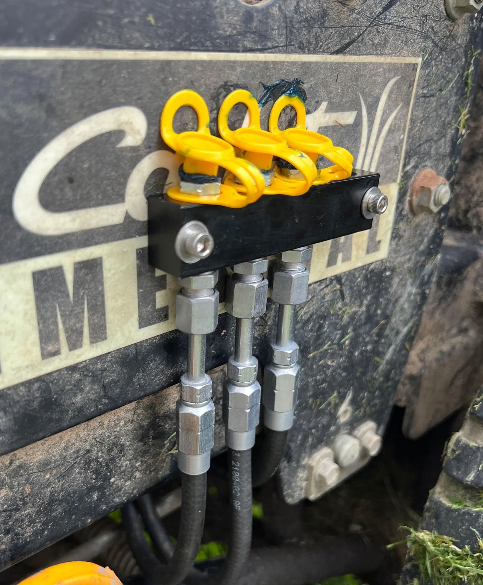 Installed yellow grease fitting caps with integrated collar on machinery, showcasing connection to metal fittings against a dirty surface.