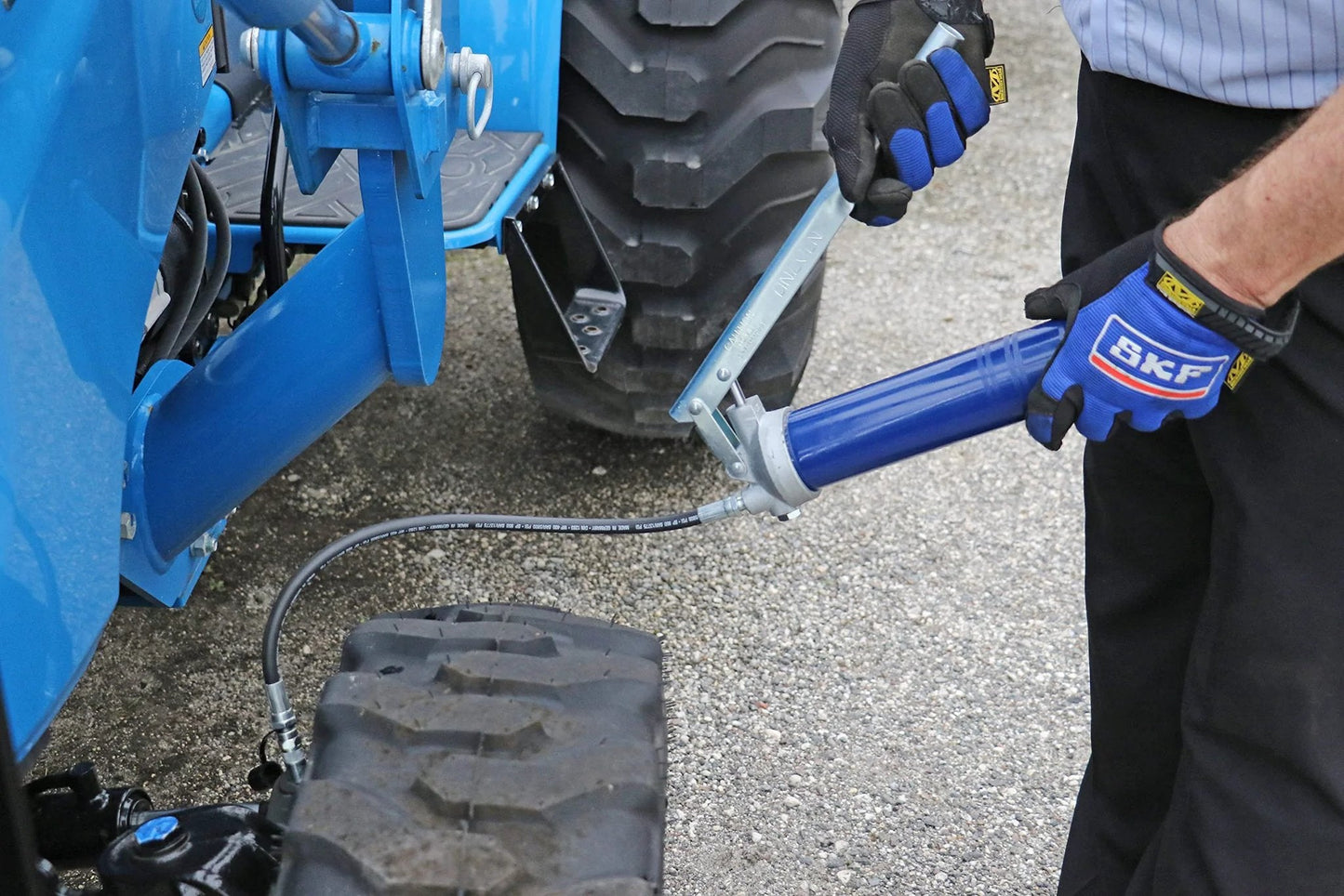 Person using Heavy Duty Lever Action Grease Gun With 18 Inch Whip Hose And Coupler, Jam Proof Toggle on farm machinery