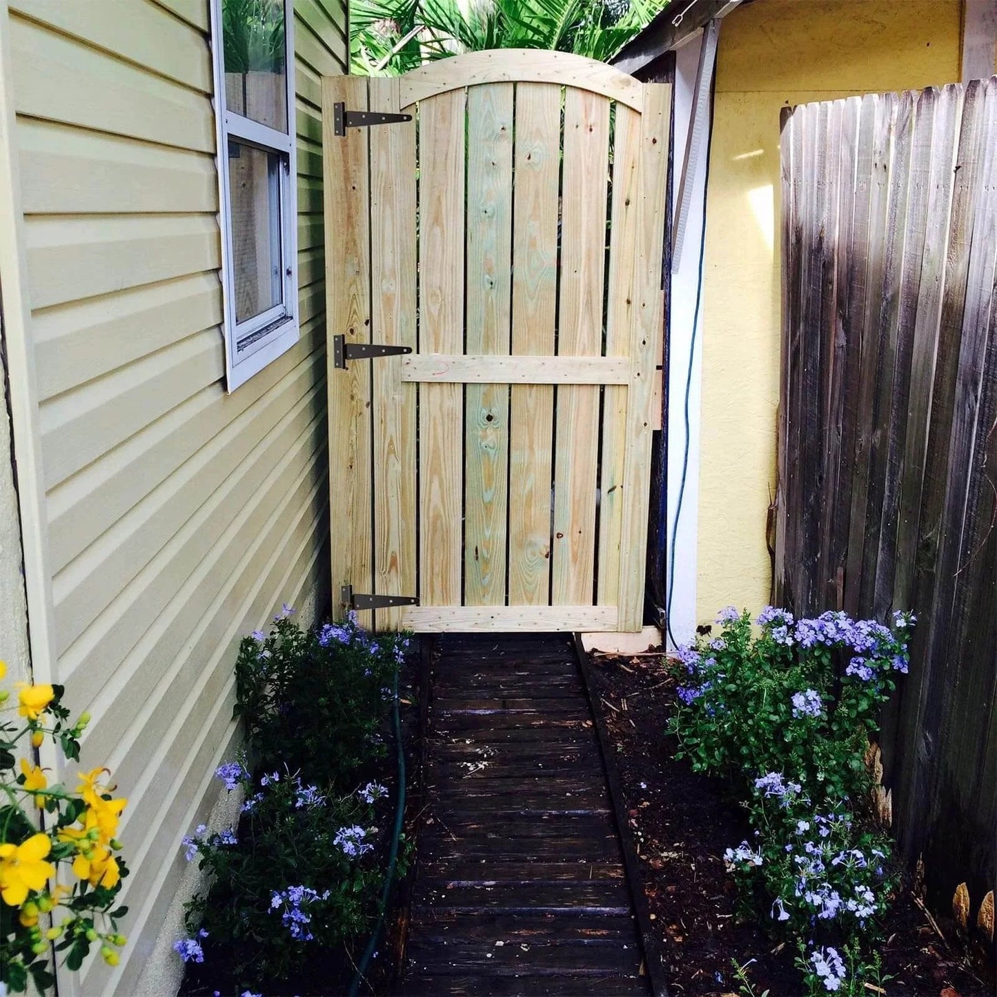 Wooden garden gate installed with 6 Pack 8 Inch T Strap Hinges Heavy Duty Shed Door Hinges Gate Strap Black Tee Hinge, surrounded by flowers.