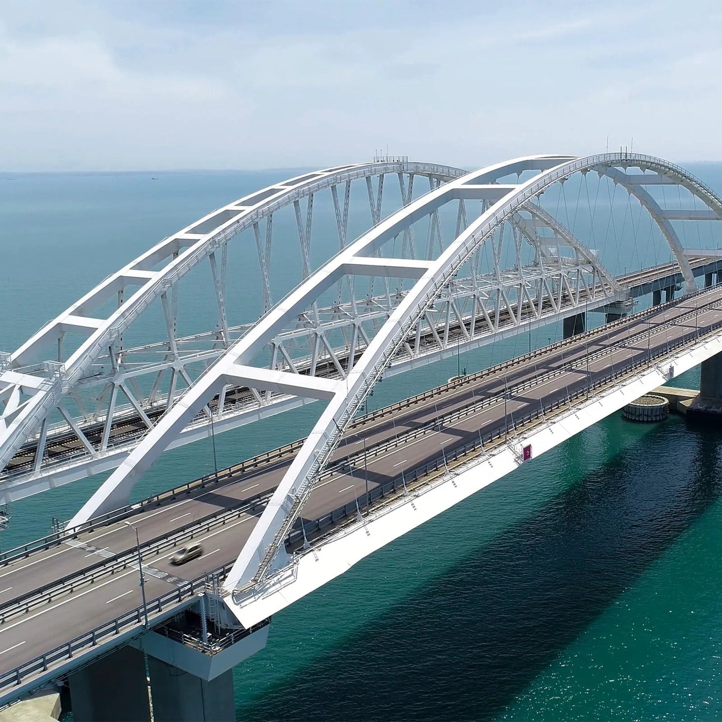 Aerial view of a large white arched bridge spanning over blue water.