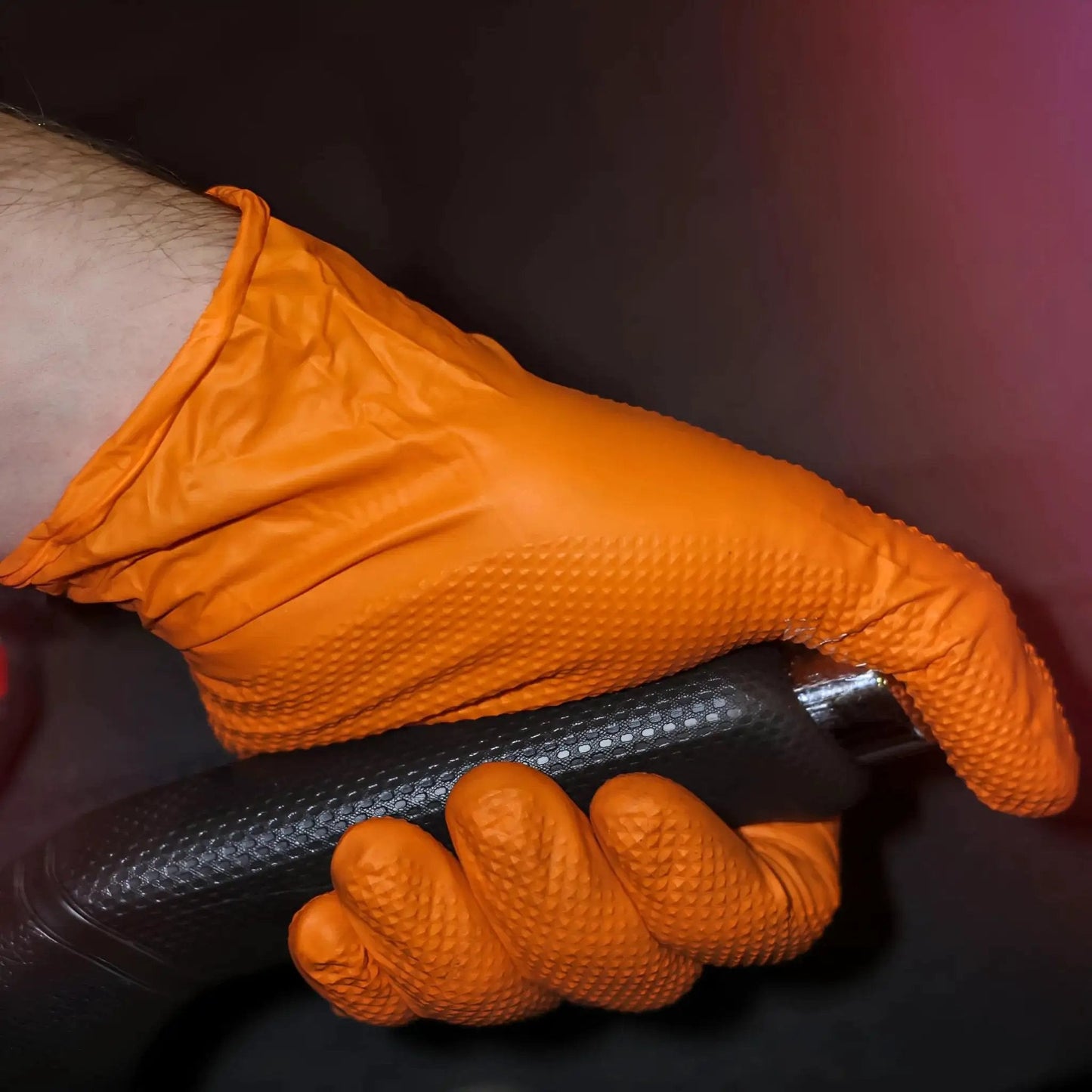 Hand wearing Heavy Duty Nitrile Gloves 8 Mil Diamond Grip Latex Free Orange XXL 100 Count holding a black tool handle