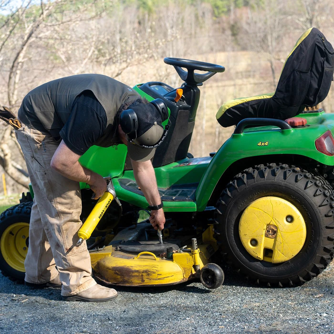 Man using Premium Pistol-Grip Grease Gun With LockNLube Coupler, 20 Inch Hose And Inline Swivel on a lawn tractor.