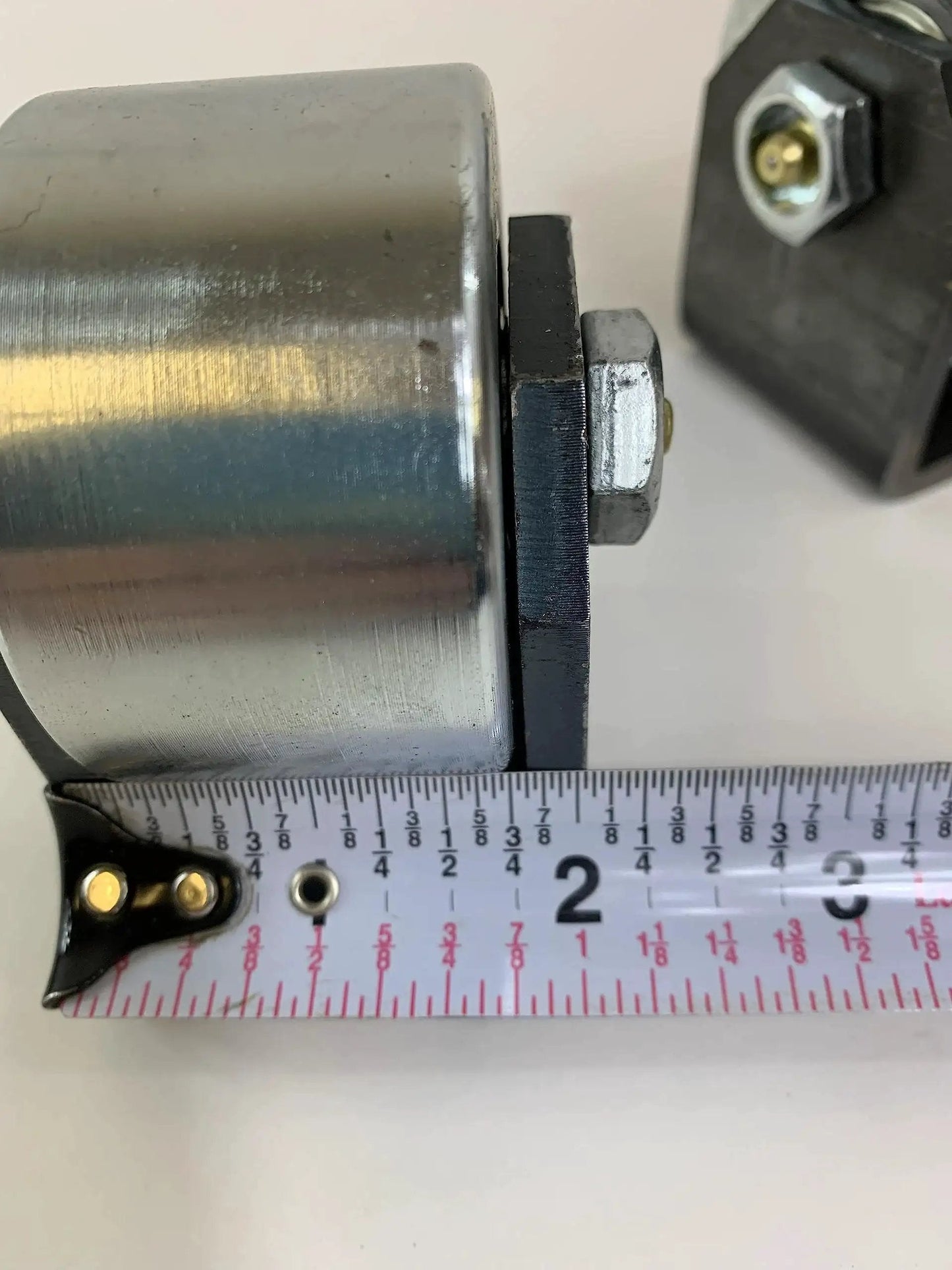 Close-up of Set Of 2 Weld On Trailer Tail Drag Casters with solid steel roller and measuring tape for size reference