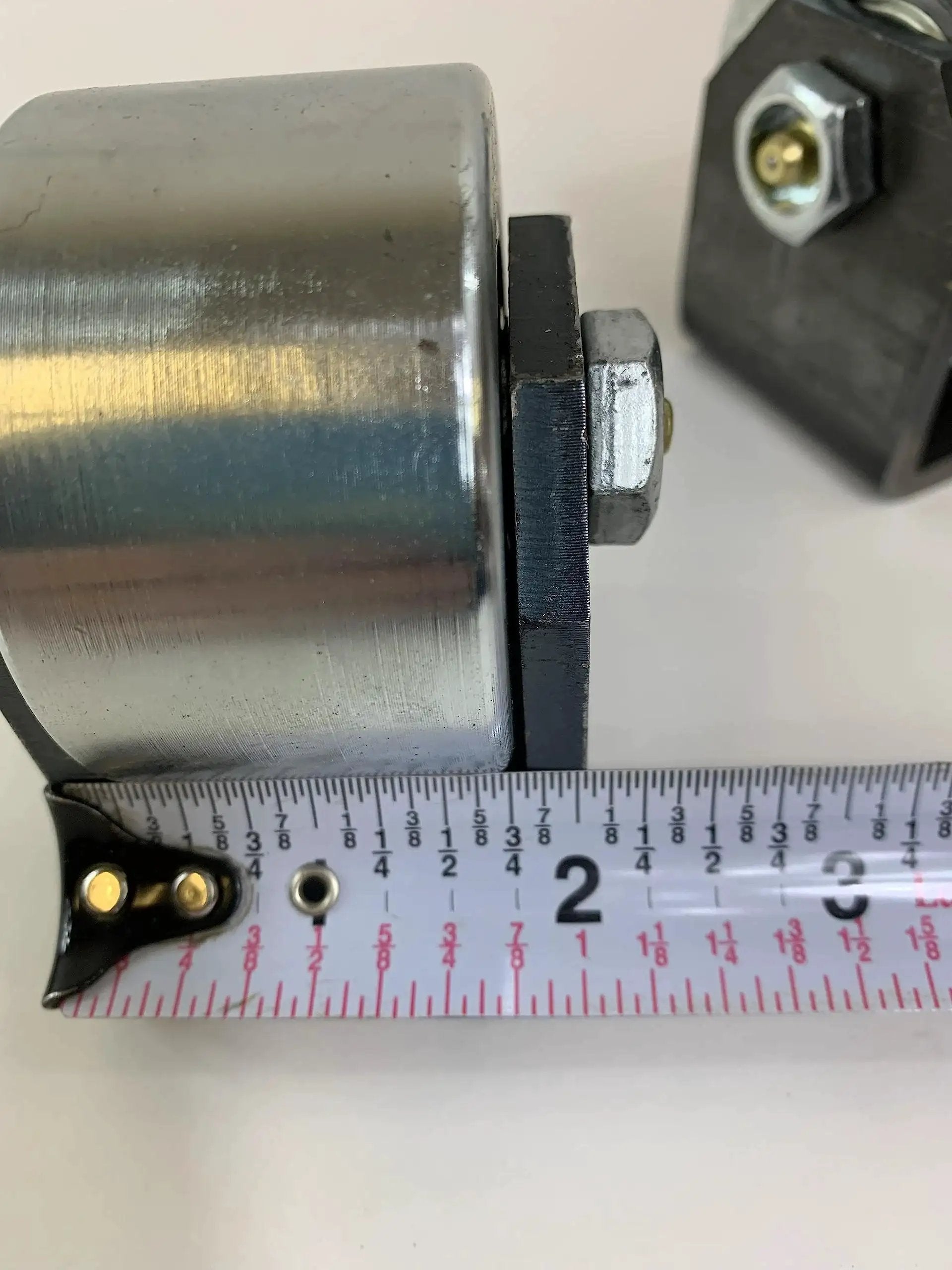 Close-up of Set Of 2 Weld On Trailer Tail Drag Casters with solid steel roller and measuring tape for size reference