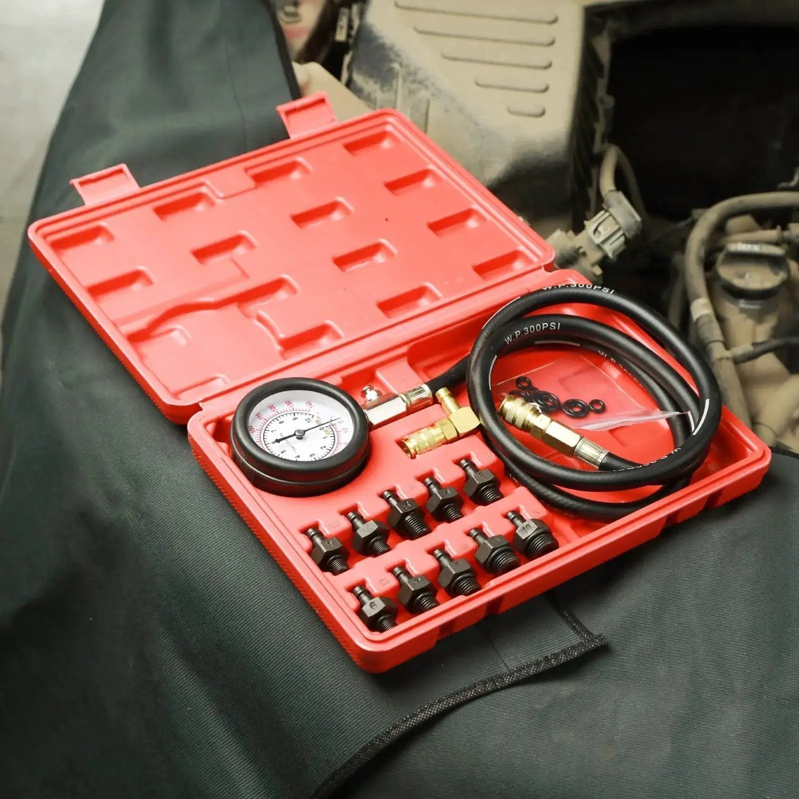 Oil Pressure Tester Kit With Dual Gauge 0 To 140 PSI 10 Adapters in red case next to engine bay