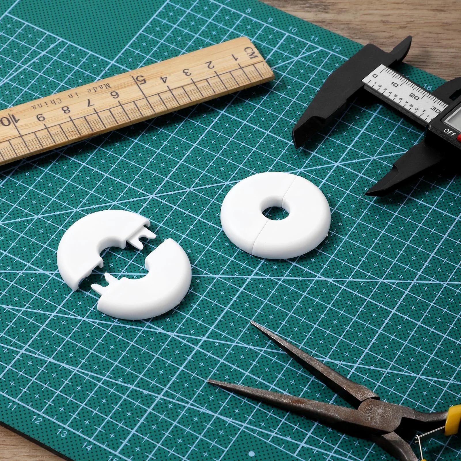 Top view of 4 Pack Wall Grommets For Cables With Adhesive Backing, Anti Slip Cable Pass Through Hole Covers For Walls And Furniture, Starlink Cable Routing Kit, Wire Holes, White shown on a cutting mat with tools.