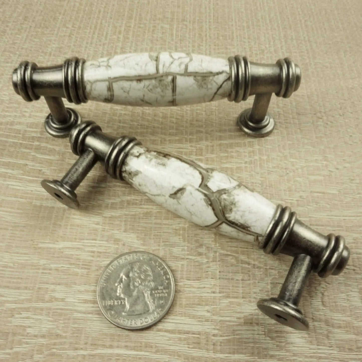 Two ornate silver gray cabinet pulls with marbled white accents, shown with a coin for scale.