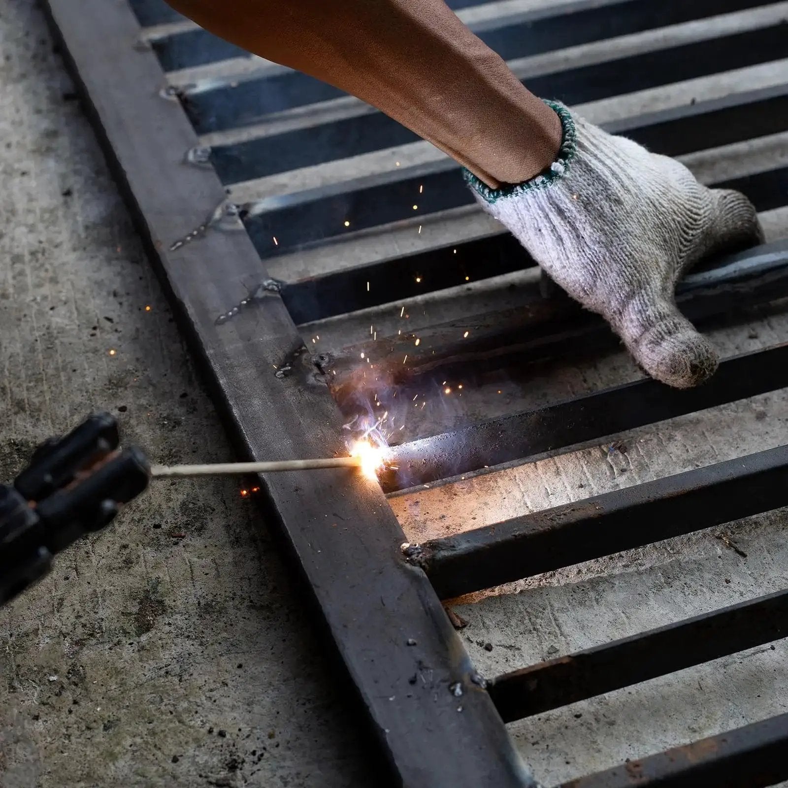 Welding a metal grid with a protective glove on, sparks flying during the process