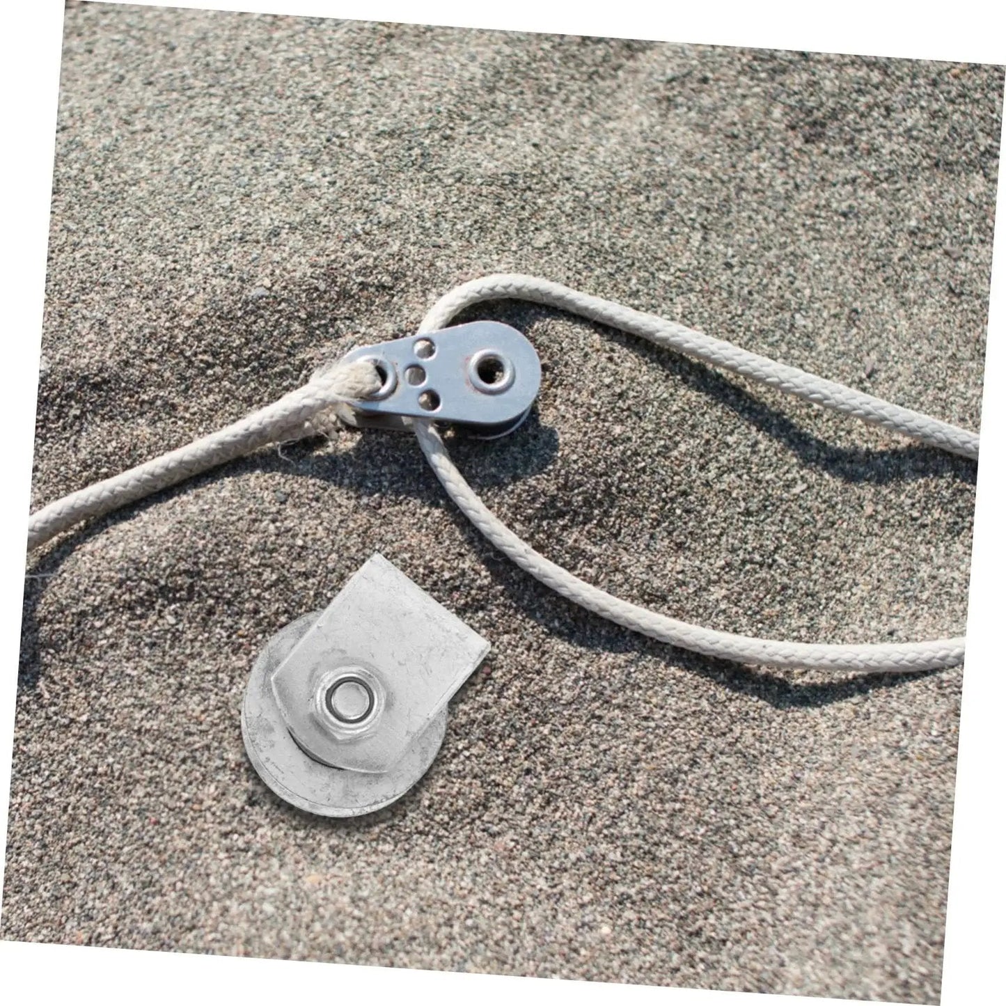 Metal pulley and rope system on sandy surface, showcasing components used in industrial cast iron groove wheel garage door roller setups.